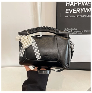 Detail of black PU leather bag with woven handle, pearl heart charm and lace bow