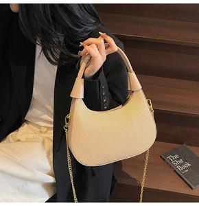 Detail of beige woven hobo bag with gold chain strap held against a lifestyle background