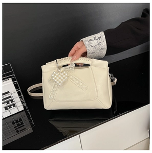 Detail of cream white leather handbag featuring pearl heart and lace bow charms