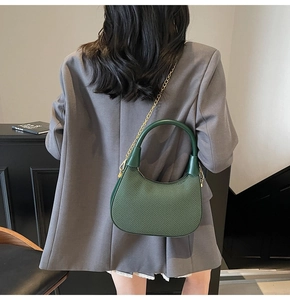 Detail of dark green woven crescent bag with gold chain strap on grey blazer