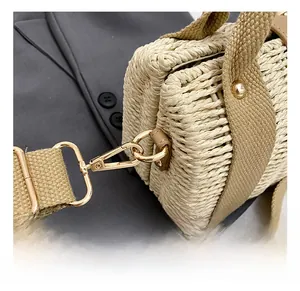Close-up of golden metal hook and thick fabric strap on a beige woven beach handbag