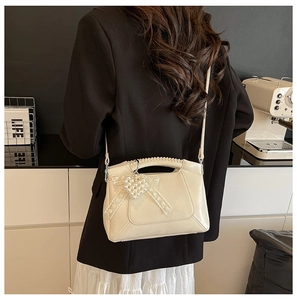 Cream shoulder bag with pearl bow charm shown on model in urban street setting