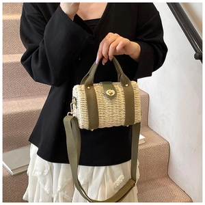 Detail of hand-woven cylindrical straw bucket bag with green canvas handles and golden twist lock