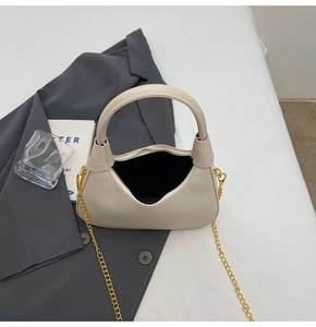 Detailed view of beige patchwork handbag with golden chain strap on a grey blazer