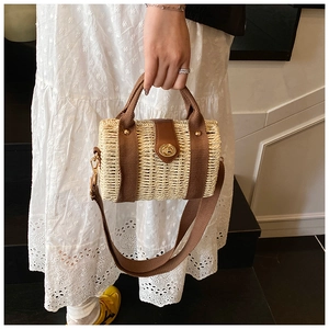 Detail of woven straw box bag featuring brown ribbon handles and metal turn-lock closure
