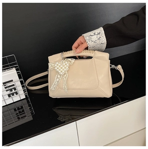 Detail of beige shoulder bag with pearl bow charm and woven handle on glossy surface