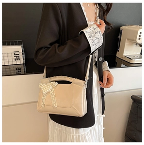 Beige crossbody bag featuring a pearl bow charm and glossy leather finish on a model