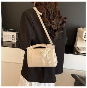 Detail of beige shoulder bag featuring a pearl bear charm and lace ribbon decoration