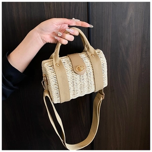 Detail of hand-held straw bag featuring beige weave, tan handles, and a gold metal twist lock