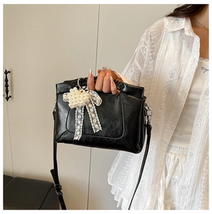 Detailed shot of black leather handbag with pearl bow and lace edge on minimalist model