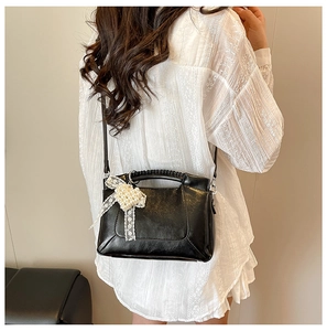 Detail of black leather crossbody bag featuring pearl heart charm and lace bow decor