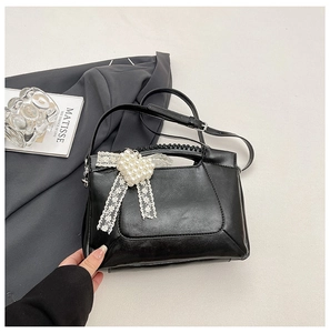 Detail of black leather handbag with pearl heart charm and lace bow decoration