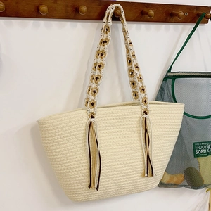 Chic beige straw woven tote bag with contrasting tassels hanging on a dark wood hook