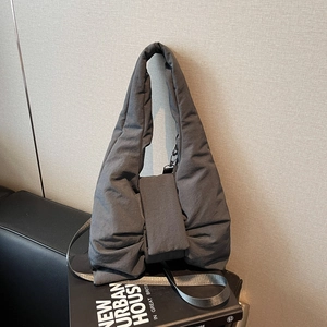 Dark grey bow-shaped quilted puffer shoulder bag with wide strap on a book background