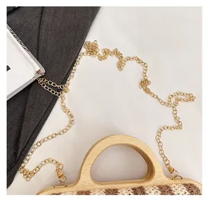 Detail of wooden handle and pale gold metal chain strap on striped woven beach tote bag
