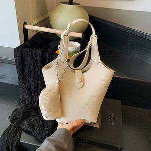 Cream lychee textured leather bucket bag with matching coin purse on a black pedestal