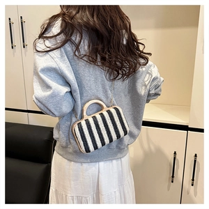 Detail of hand-woven straw bag featuring black stripes and round wooden handles