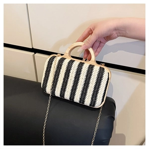Detail of woven straw bag with black stripes and natural wooden handle with gold chain