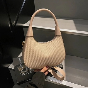 Minimalist beige woven leather handbag with gold chain on stone background