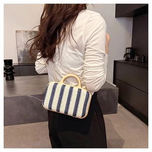 Detail of hand-woven blue and white striped straw bag with round wooden handle and gold chain
