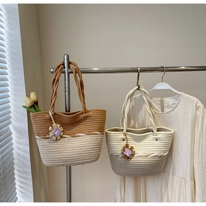 Detail of woven straw tote bags with floral charms hanging on a metal rack