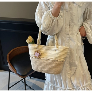 Detail view of a woven tote bag featuring cream and brown texture and a flower charm