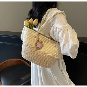Detail of woven tote bag with purple floral charm shown on model for resort vacation