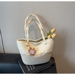Detail of woven tote bag featuring floral charms and rope handles on a design book