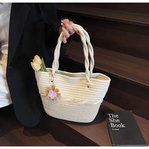 Detail of woven tote bag featuring a floral charm and twisted handles on wood steps