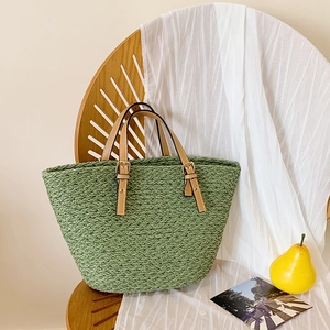 Close-up of green woven straw tote bag with brown leather handles and gold metal buckles