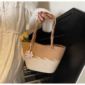 Detail of woven straw tote bag with dual-tone brown and beige design and floral charm