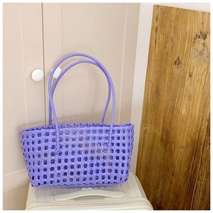 Détail d'un sac cabas tissé violet ajouré posé sur une valise pour l'été