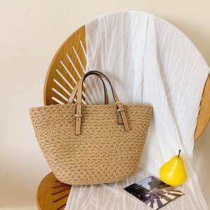 Detailed texture of woven straw tote bag with brown leather strap and golden buckles