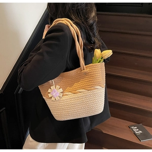 Detail of woven straw tote bag with bicolor texture and purple flower charm accent