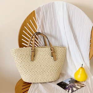 Close-up of handwoven straw tote bag with brown faux leather handles and gold metal buckles