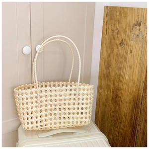 Gros plan d'un sac à main tissé ajouré beige minimaliste posé sur une valise