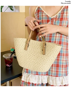 Close-up of beige woven tote bag with brown leather handles and golden metal buckles