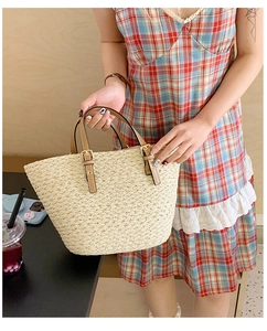 Detail of summer woven straw tote bag featuring brown leather handles and golden buckles