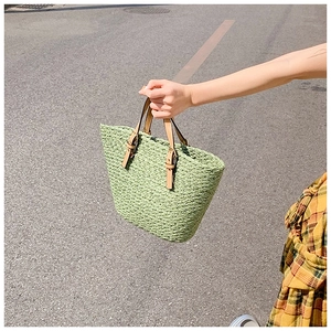 Detail of light green woven straw tote bag with adjustable leather handles and metal buckle