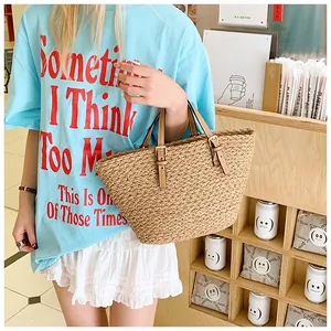 Detail of woven straw tote bag with brown leather handles and adjustable metal buckles