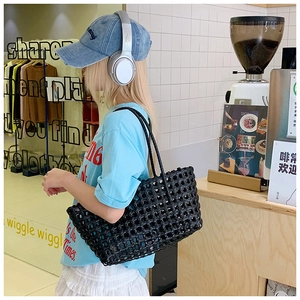 Vue détaillée d'un sac cabas noir tressé ajouré porté par un mannequin dans un café chic