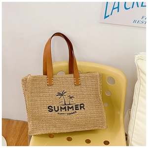 Close-up of woven straw tote bag with palm tree embroidery and leather handles