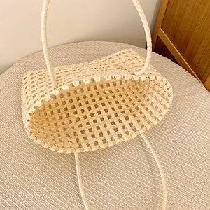Vue de dessus d'un sac à main tissé crème ajouré avec longues anses tressées sur socle clair
