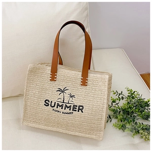 Close-up of woven straw tote bag with brown leather handles and summer embroidery