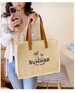 Detail of woven straw tote bag with palm tree print and leather handles in use