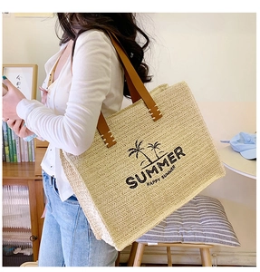 Detail of woven straw tote bag with palm tree pattern and brown leather handles