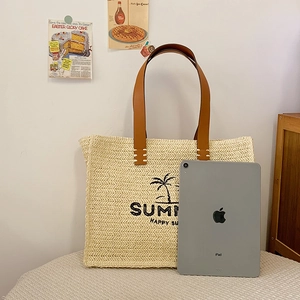 Detail of woven straw tote bag with palm tree print and brown leather handles on a beige surface