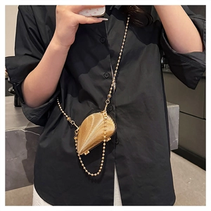 Detail of a golden seashell-shaped metal evening bag with fine radial engraved lines