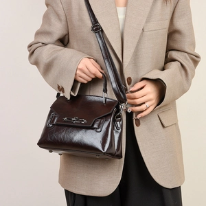 Détail du sac à bandoulière en cuir brillant marron foncé avec texture huileuse et fermoir métal