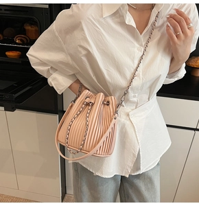 Detail of pink pleated drawstring bucket bag with silver chain strap shown in a home setting
